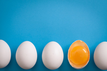 White eggs is laying in row, one of them is bisected and shows yolk.