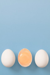 White eggs is laying in row, one of them is bisected and shows yolk.