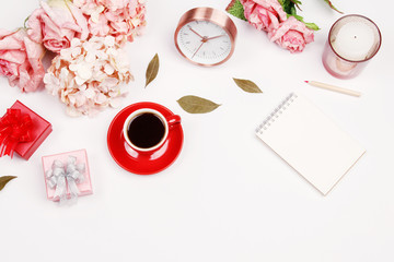 Valentines day background. Feminine desk workspace frame with pink beige floral bouquet, red coffee cup, candle, gift box and notebook on white background with copy space. Flat lay. Top view.