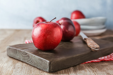 Wooden board with ripe red apples on table