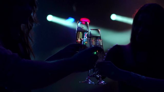 Clinking glasses of champagne in hands on bright lights background. Silhouette of a group of friends with glasses of champagne in the dark against the bright flashing lights.