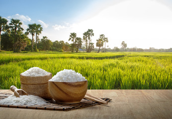 Fototapeta na wymiar Jasmine rice and steamed rice in wooden bowl with the chopsticks on the wooden table with the plantation rice at sunset