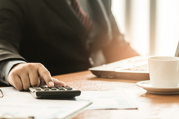 A businessman analyzing investment charts at his workplace and using his laptop and touch calculator.