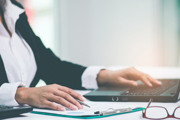 A business woman's hand holding pen pointing on summary report chart and calculate finance in office.