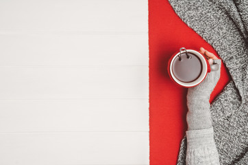 Female hand holding a cup of tea or coffee on white wooden table. Winter or christmas cosy background. Photograph taken from above, top view with copy space