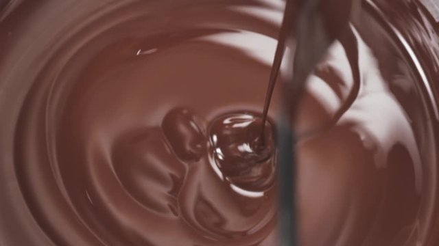 Slow motion top view stirring and pour dark melted chocolate