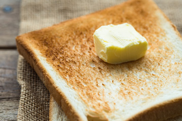 piece of fresh butter on stacked toasted slice sandwich bread on gunny sack cloth on wooden table, close up