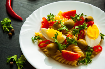fusilli pasta salad with tomato, eggs and olive in plate on dark wooden background