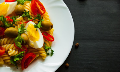 fusilli pasta salad with tomato, eggs and olive in plate on dark wooden background