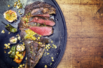 Australian barbecue dry aged wagyu tomahawk steak with vegetable and fruit relish as close-up on an old board