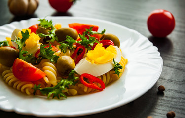 fusilli pasta salad with tomato, eggs and olive in plate on dark wooden background