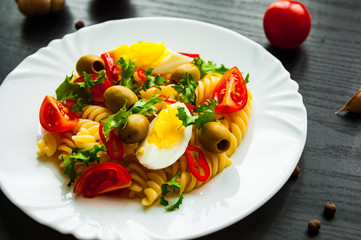 fusilli pasta salad with tomato, eggs and olive in plate on dark wooden background