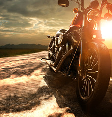 old retro motorcycle traveling on country road against beautiful light of sunset sky