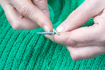 Close up view of a elderly woman hands who knits a green sweater