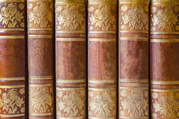 Old closed brown books with gilded patterns  in a row as background, texture