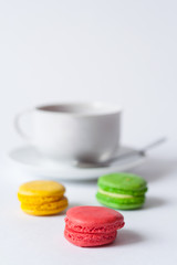 Obraz na płótnie Canvas Traditional french multicolored cakes macarons in the foreground and a cup of tea on a saucer in a blur on a white background