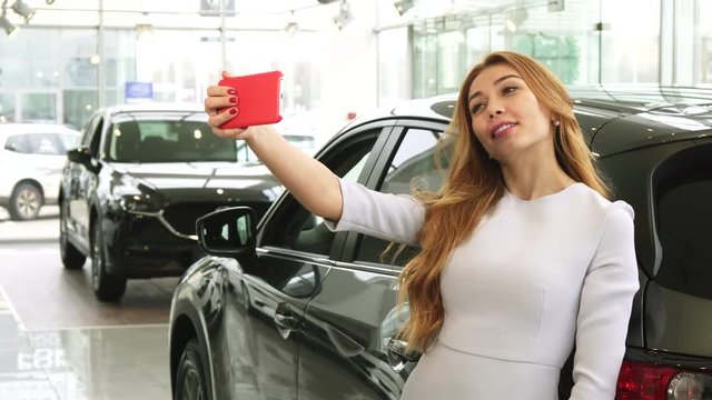 Young beautiful happy woman smiling cheerfully using her smart phone taking selfies with her newly bough automobile at the dealership customer buyer driver luxury lifestyle