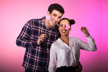 Happy inlove couple with pink hearts in their hands on pink background in studio