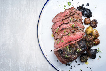 Barbecue caveman wagyu roast beef sliced with mushrooms and potatoes as top view on a tray with copy space left