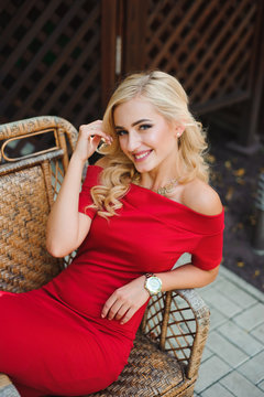 Fashionable attractive blonde woman in red dress sitting on chair.