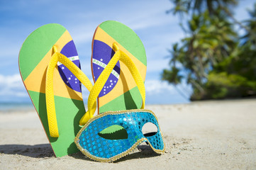 Brazil flag flip-flops and brightly sequined carnival mask resting together in the sand on the...