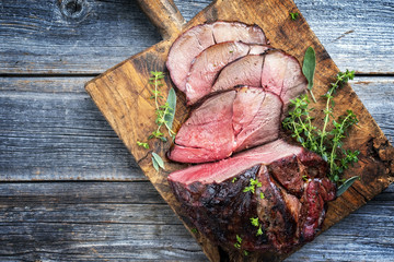 Barbecue dry aged Hirschkeule mit Kräuter als  close-up auf alten Schneidebrett