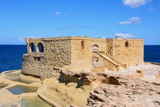 Salt pans and the Il-Qolla I-Badja battery along the waterfront, Marsalforn, Gozo, Malta.