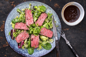 Barbecue wagyu point steak slices with mixed lettuce and hot sauce as top view on a plate