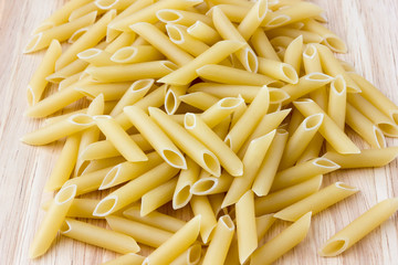 Raw macaroni of hard varieties on a wooden table. A pile of macaroni penne scattered on a close-up table.