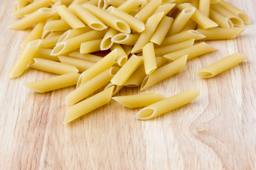 Raw macaroni of hard varieties on a wooden table. A pile of macaroni penne scattered on a close-up table.