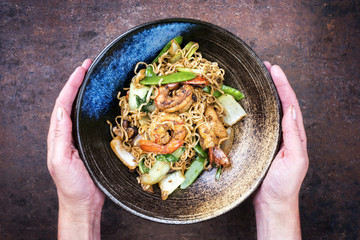 Traditional stir-fried Thai phat phak kung with mie noodlesas top view in a bowl in woman hands