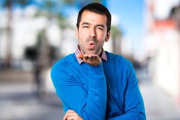 Handsome young man sending a kiss on unfocused background