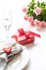 Valentines day dinner with table place setting with red gift, glass for champagne, heart ornaments with silverware. Valentine's card.