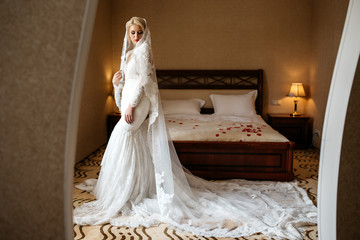 Beautiful bride in a lace wedding dress and a long veil standing in hotel room