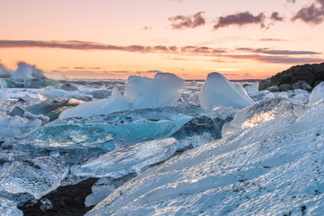 Fototapeta na wymiar The sun rises over the Atlantic Ocean illuminating the famous Icebergs on Diamond Beach, at the opening of Jökulsárlón glacier lagoon