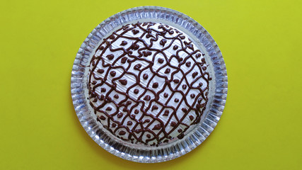 Cake decorated with chocolate coating on yellow background
