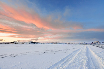 Fototapeta na wymiar The sunsets and reflets off the clouds creating very vivid cloud patterns over tracks in the snow left by an oversize 4x4 vehicle invoking a sense of adventure