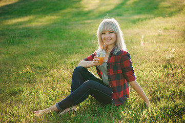 Fototapeta premium Beautiful girl with an orange cocktail on the grass in the park