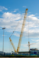 Fototapeta na wymiar High building under construction. Side with cranes against blue sky with sun glare.