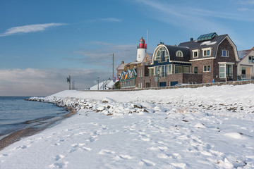 Winter landscape with Dutch beach covered with snow and view at lighthouse of fishing village Urk