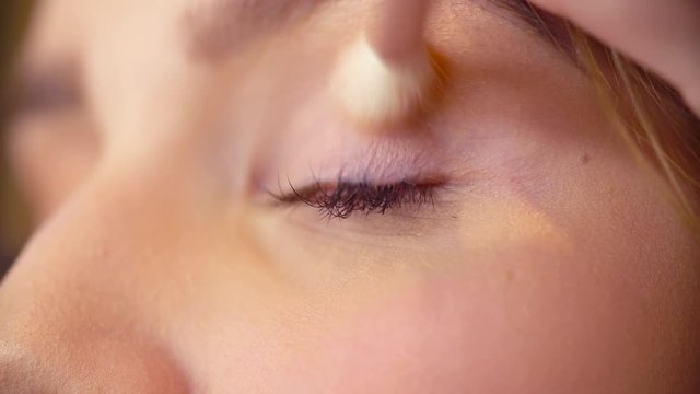 Extreme close up of the female eyes. Professional makeup artist applying eyeshadow on the eyes of the model with special brush