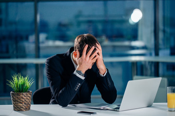 Stressed businessman having problems and headache at work sitting with laptop