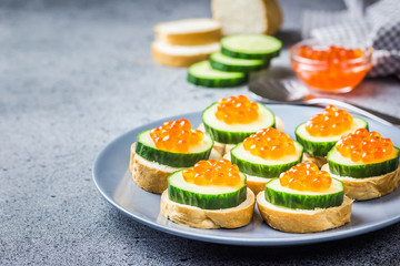 Red caviar cucumber appetizer on concrete background. Selective focus, space for text. 