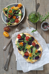 Flammkuchen mit blauen Kartoffeln, bunten Tomaten, Rucola und Rucolapesto