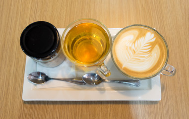 Coffee late art in cup and sugar bottle and tea cup on white plate on woden table