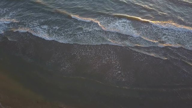 waves gently lap over clean sand at sunset, aerial shot