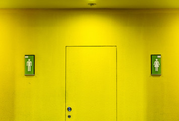 yellow wall in front of toilet with sign or symbol of Man and Women.