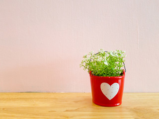 small mock up or fake plant in the red pot with white heart sign on the wooden table with pink wall background.