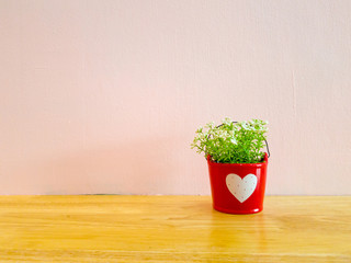 small mock up or fake plant in the red pot with white heart sign on the wooden table with pink wall background.