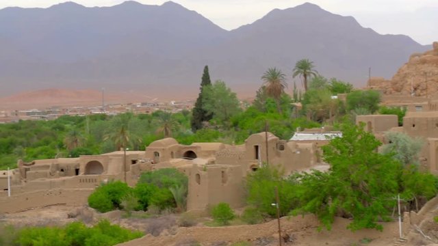 old adobe village located in an oasis at sunset, around a deserted place, in the distance a long ridge